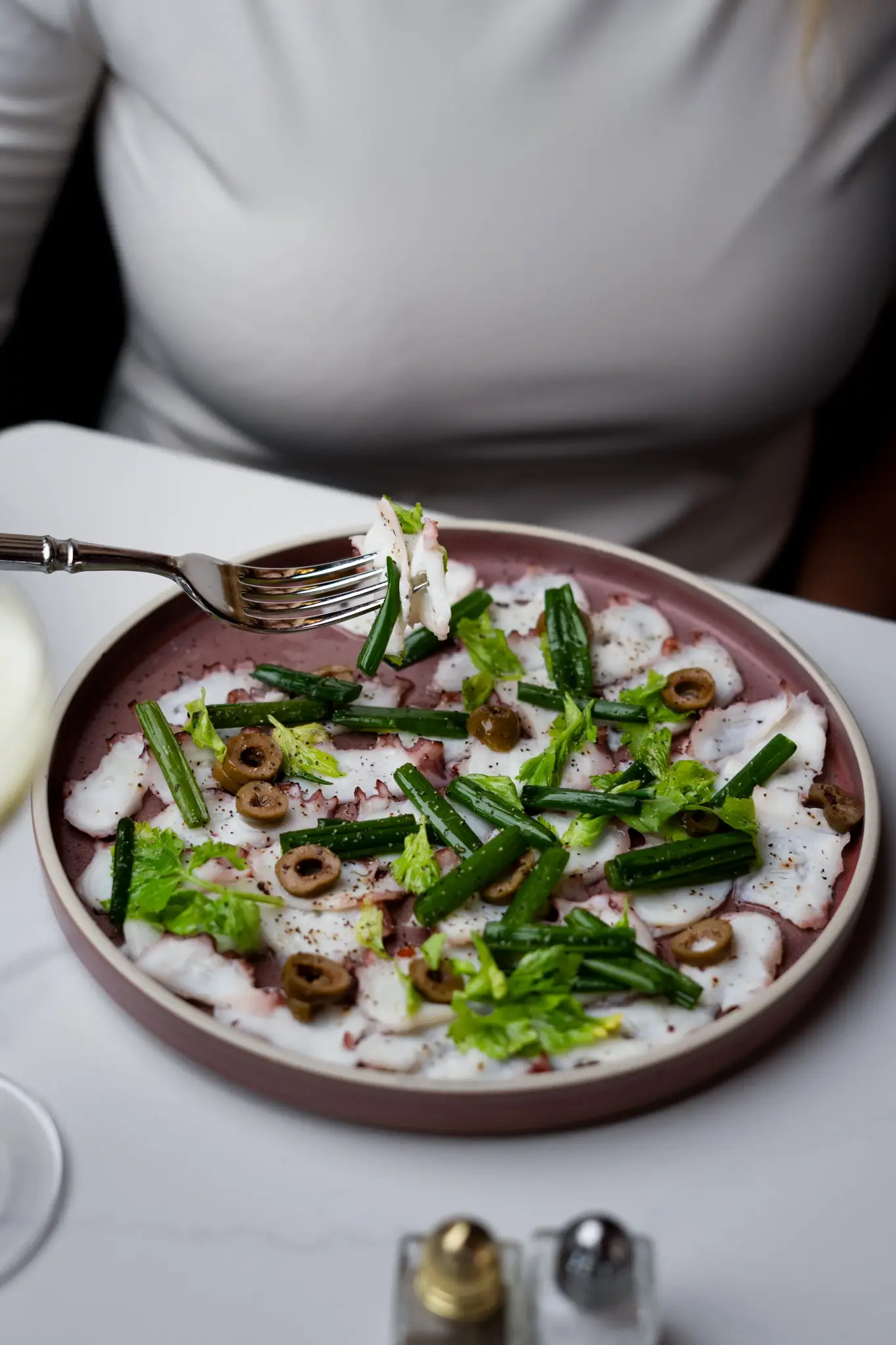 Octopus carpaccio sliced thin with olives and herbs on a plate at Siena, Alpharetta