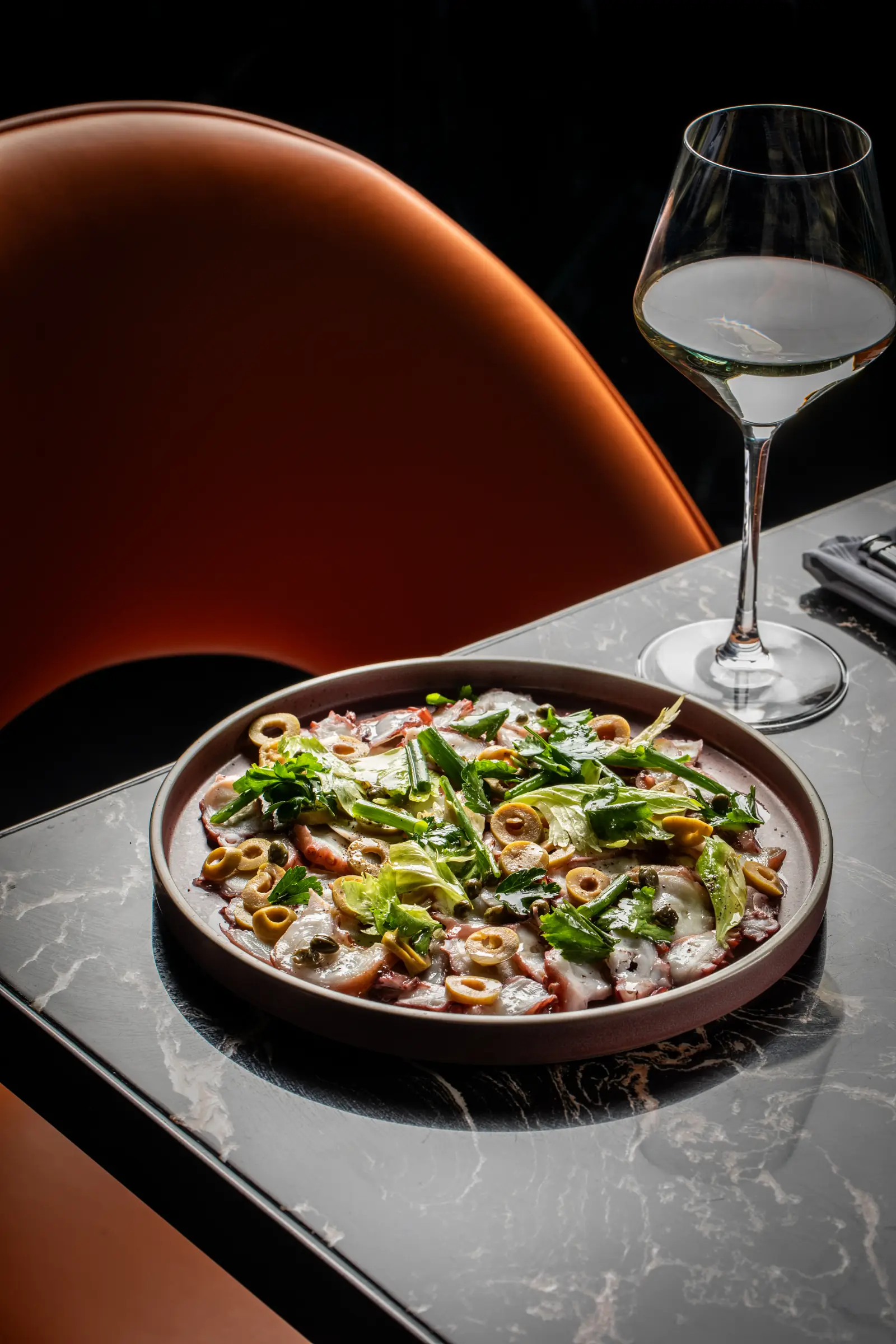 Octopus carpaccio and a glass of white wine on a marble table at Siena in Alpharetta