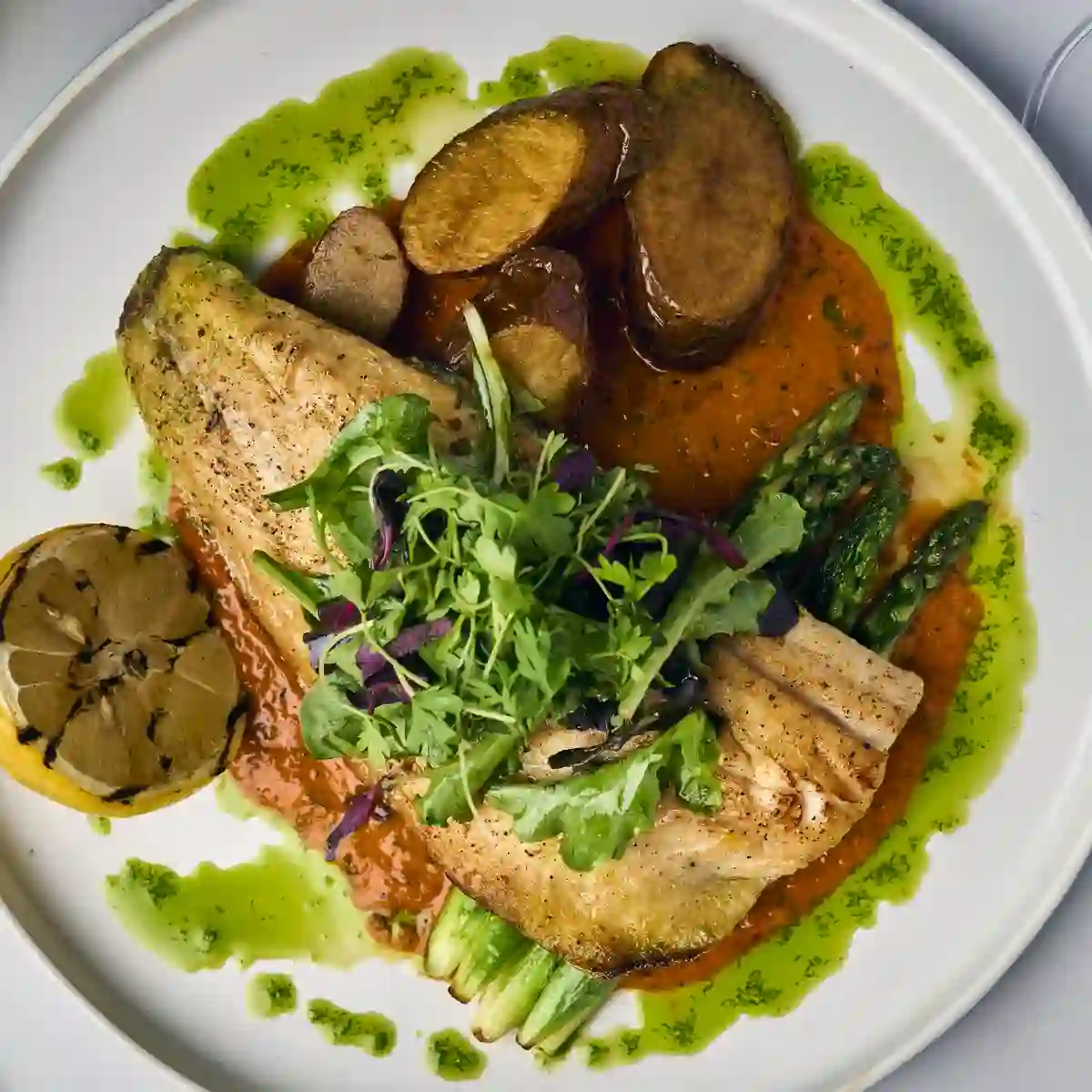 Mediterranean Branzino fillet over roasted red pepper sauce with potatoes and greens